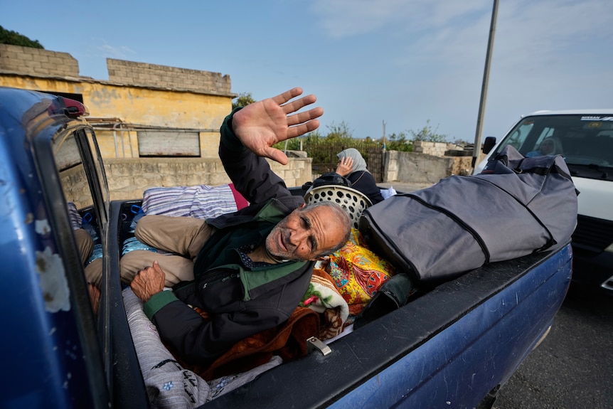 A displaced man gestures lying over belongings on a mini pickup, in Qasmiyeh Lebanon as he returns his family to their village
