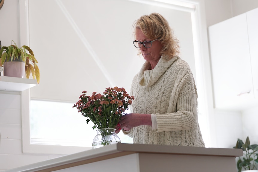 A woman arranges flowers in a vase.