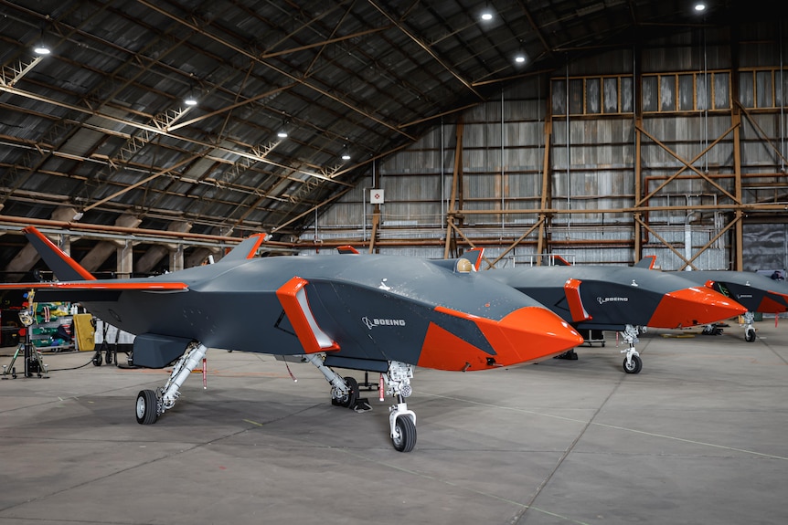 Three drones that look like aeroplanes are lined up in a hanger.