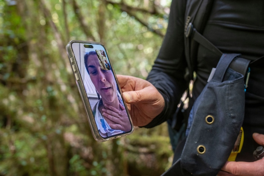 Justine on Facetime call phone with Gabriel in the forest. His hand holding the phone can be seen