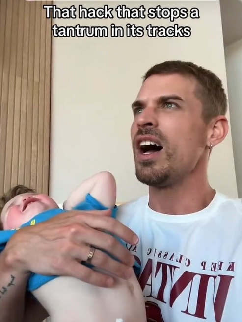 A man holding a small boy who is throwing himself around