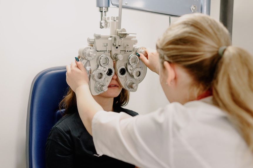 An optometrist tests a patient's eyes with an elaborate-looking apparatus.