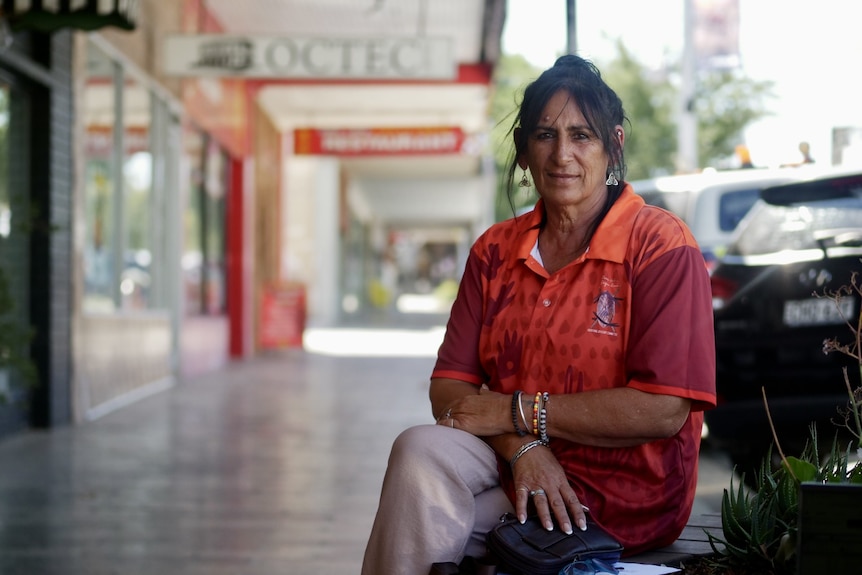 A woman dressed in red sitting down on a bench on a quiet shopping street