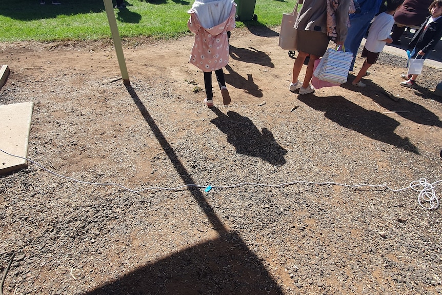 People stand close to a white extension cord that is lying across a gravel path.
