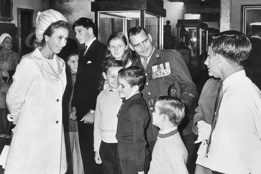 A black and white photo of a man in uniform speaking with a group of people