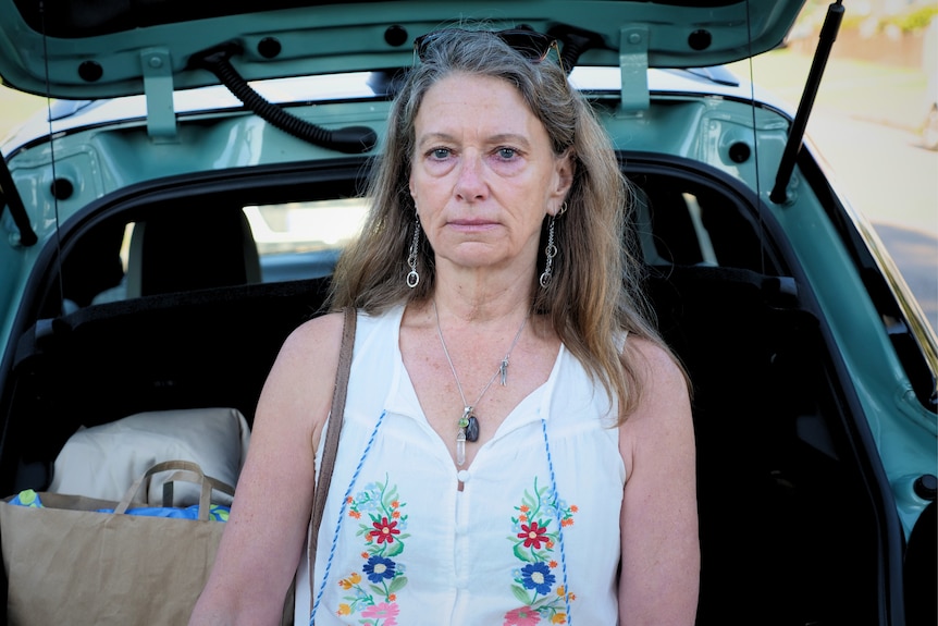 A woman leaning on the boot of her car, looking at the camera. The boot is filled with bags.
