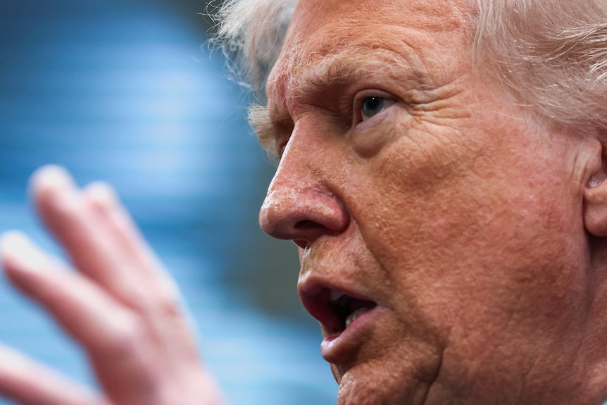 A close up of Donald Trump's face as he speaks and gestures with his hand at a podium.
