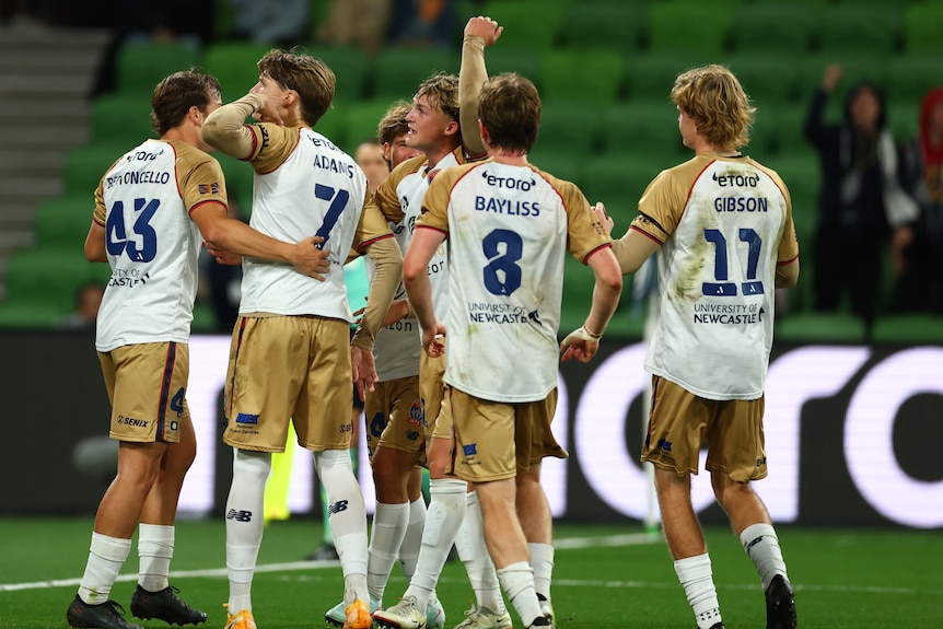 A group of soccer players in gold and white huddle and celebrate a goal