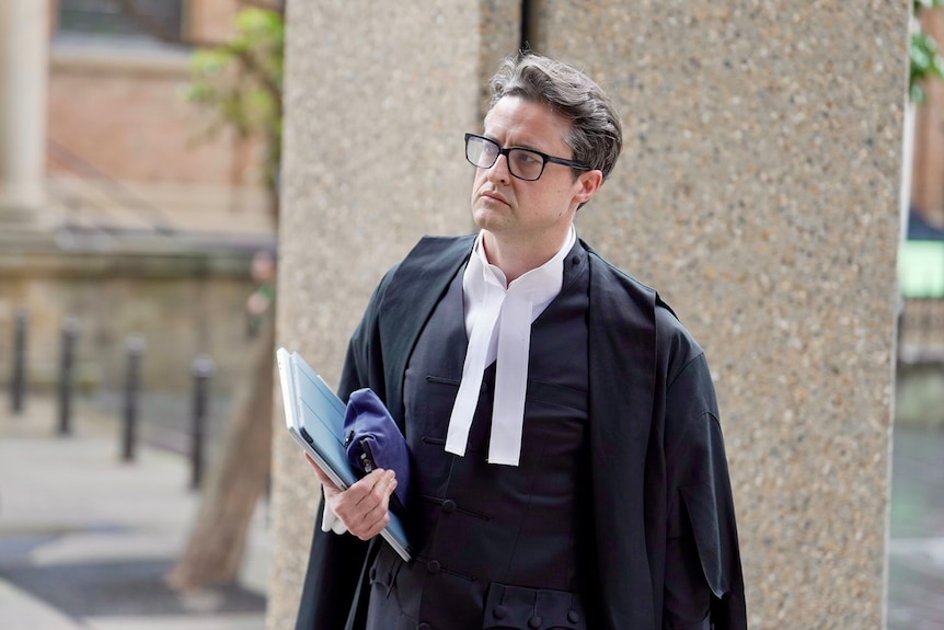 A man in court dress and glasses carries documents as he walks into court.