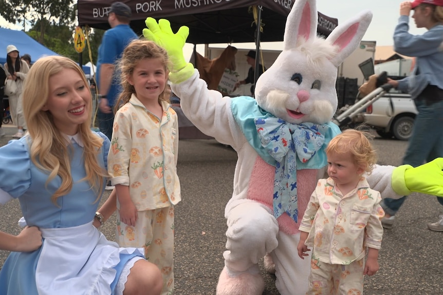 Easter bunny and a woman in costume pose next to two children in similar pajamas at an outdoor market