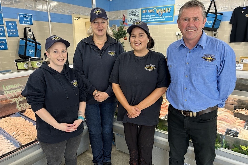 A team of colleagues stand together in front of the seafood cabinets at the Lakes Entrance Fishermen's Co-op