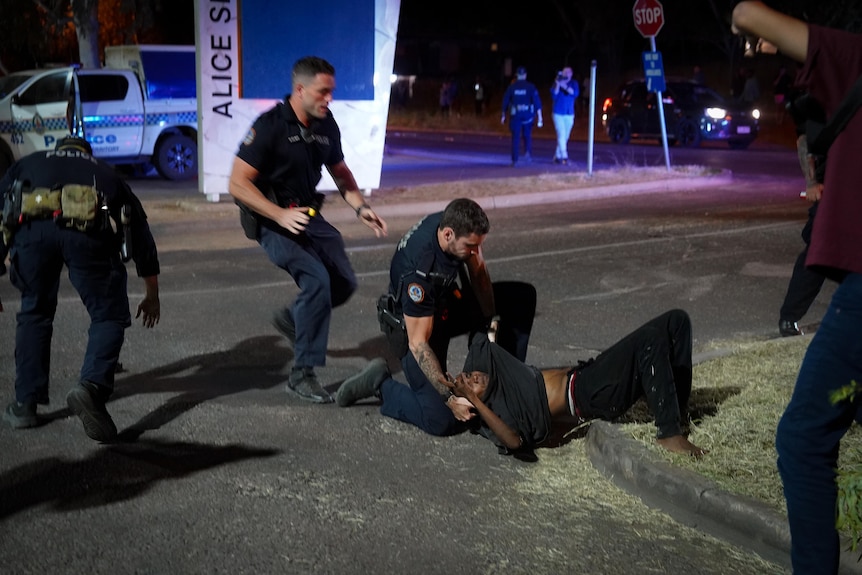 A person being arrested by two police at night out the front of the Alice Springs Hospital.