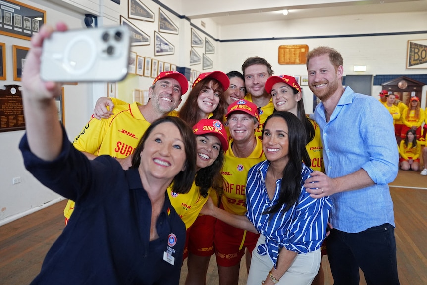 Harry and Meghan pose with a group of surf life savers inside a surf club.