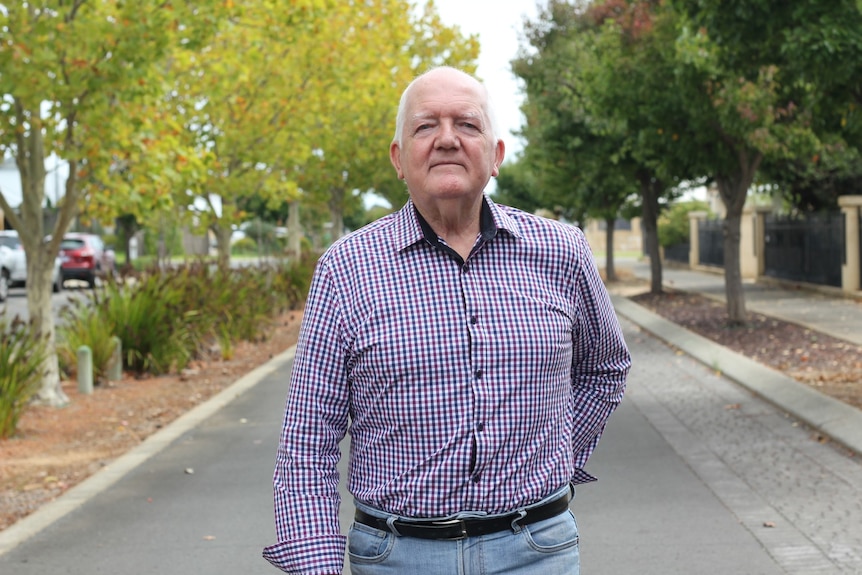 A man standing on the street, it's autumn and there are leaves in the background