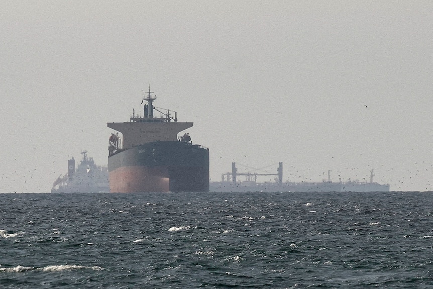 Multiple large ships on the horizon, with fog and dark blue water and a grey sky.