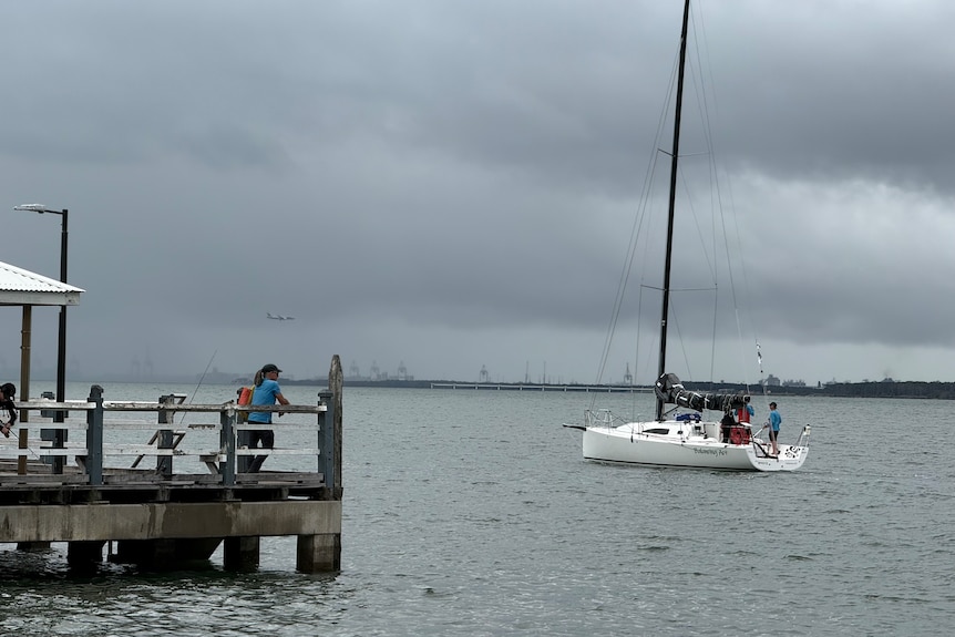 A yacht in the water next to a pier on a grey day
