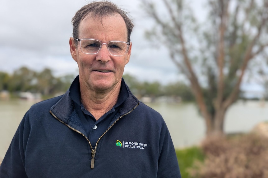 A fair-skinned man with clear-rimmed glasses smiles on the banks of the Murray River.