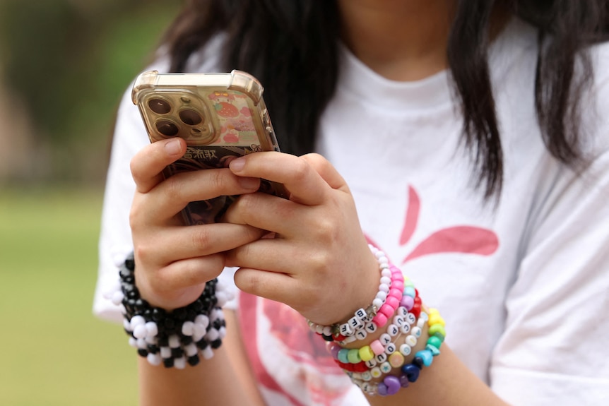 A teen wearing colorful beaded bracelets holds up a phone