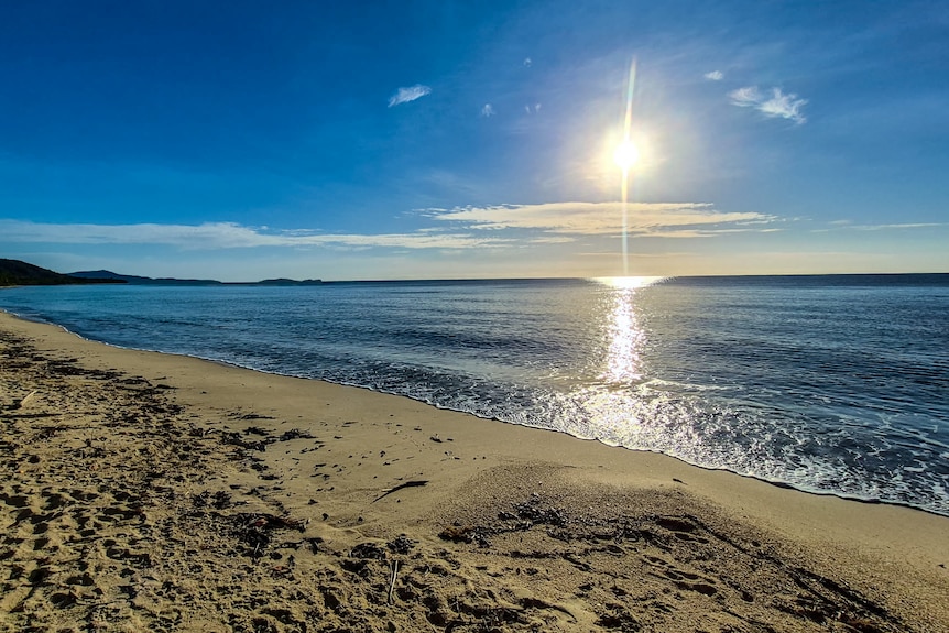 A sunrise with blue skies over a calm beach.