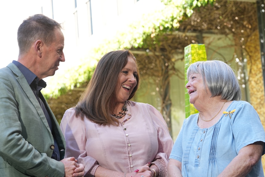 Two women and a man stand outdoors laughing together.
