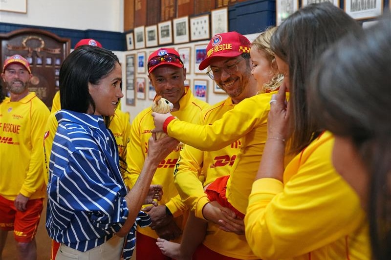Meghan grabs a toy bear being given to her by a young girl in a surf life saving uniform.