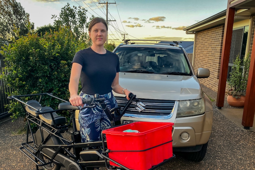 Rachael Guinman stands holding her e-bike in front of a car, Toowoomba, April 2026.