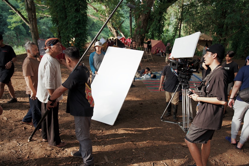 An actor standing in a forest with a film crew around him.