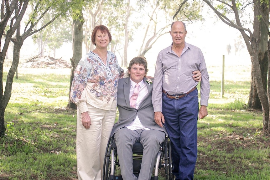 A man in a wheelchair at the center of the image with an older woman and older man on either side of him.