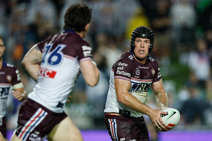 A rugby player wearing a padded black helmet looks to pass the ball.