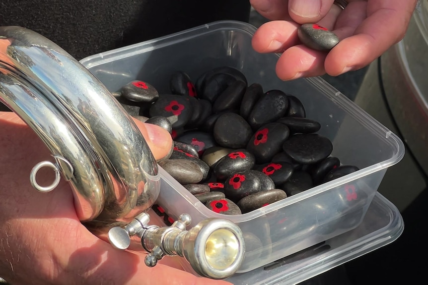 Hands holding a plastic container filled with painted rocks and a silver horn