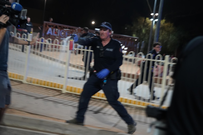 A Northern Territory police officer using pepper spray on a street at night.