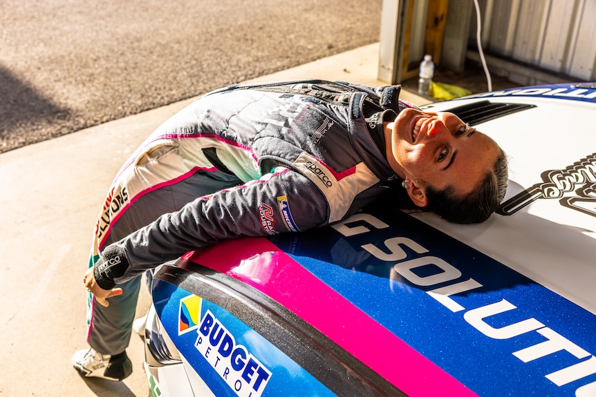 Imogen Radburn wears her racing outfit and leans on her car in a garage.