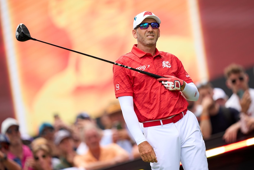 Golfer on the tee, looking at the ball after his drive, holding the club across his chest