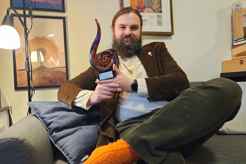Bearded man holding a black, blue and red trophy.
