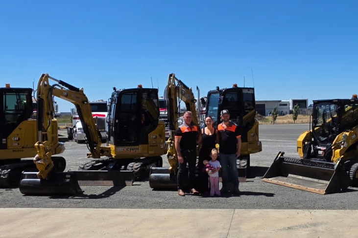 A group of people standing with earth moving equipment. 