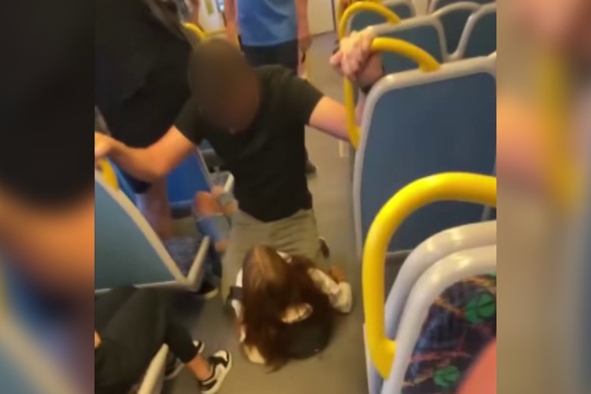 A man uses his keen to hold in place a young girl lying down one the floor of a train carriage. 