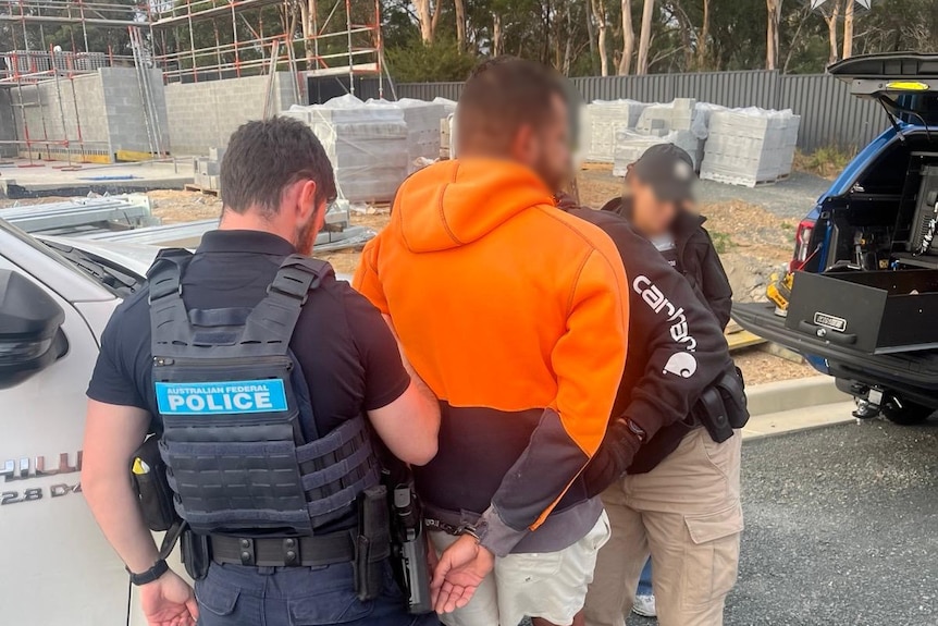 A man in hi-vis clothing is led away by police