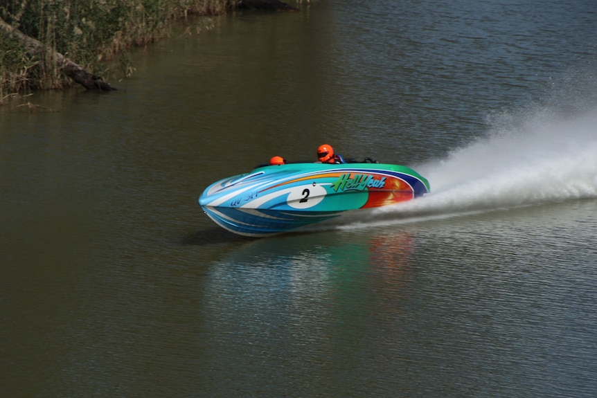 A blue speed boat skims across a glassy surface, trailing a tail of fine spray. 
