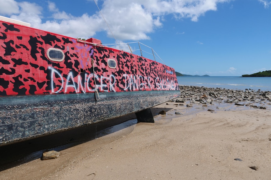 A wrecked boat on a beach with "stay away" written on its side.