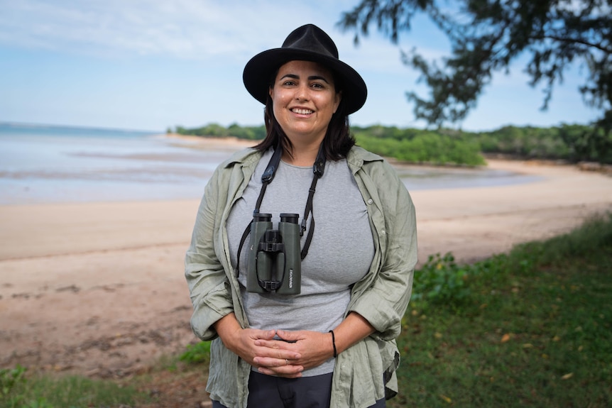 A woman wearing a wide-brimmed hat has binoculars hanging from a lanyard around her neck.