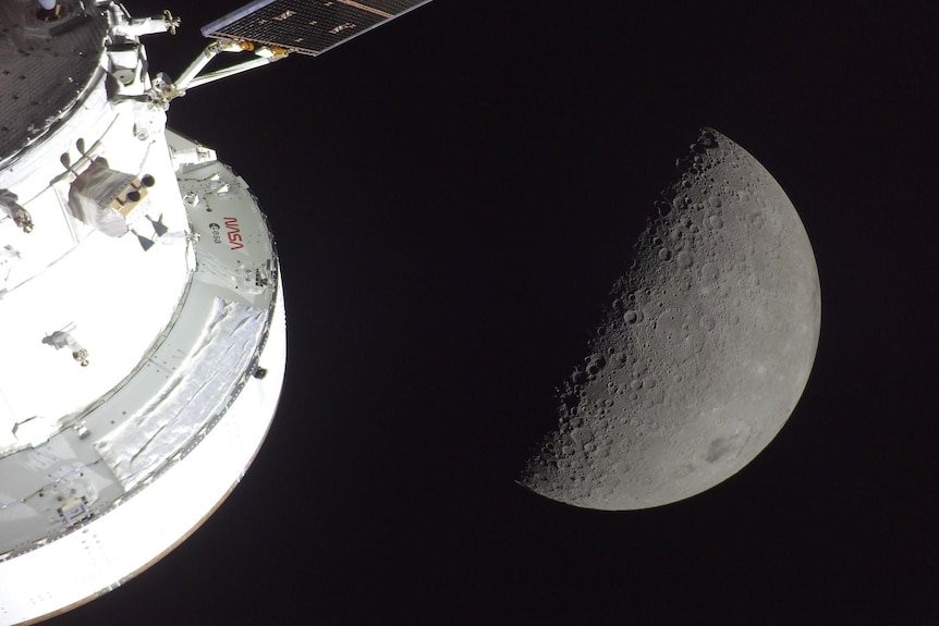 The Orion spacecraft is seen in the foreground, lit up by the Sun. A first quarter Moon is visible behind it