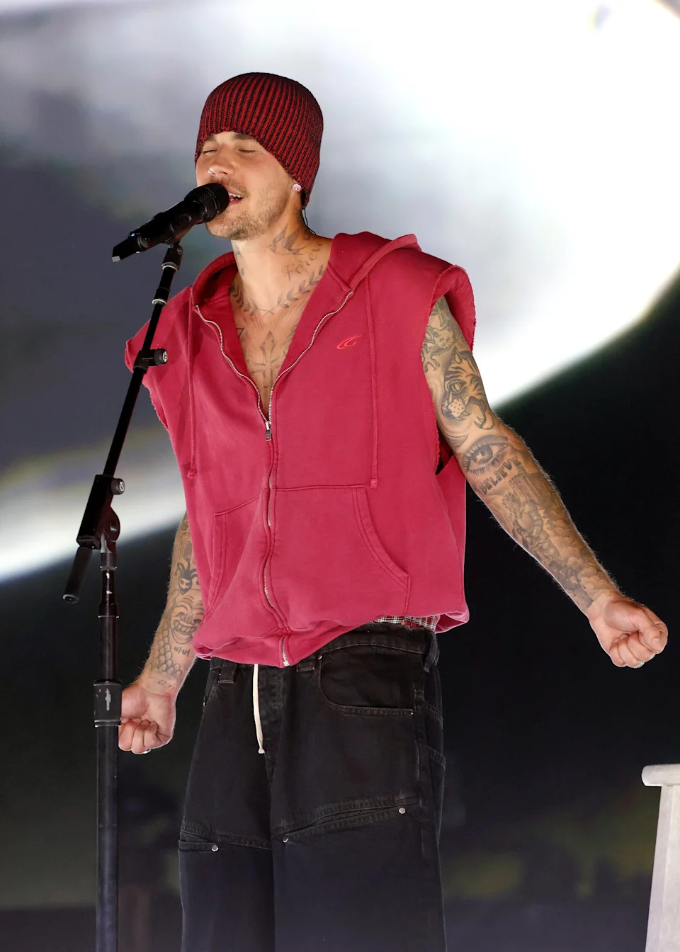Justin Bieber wears a sleeveless hoodie and pants, singing passionately at Coachella with a microphone in hand