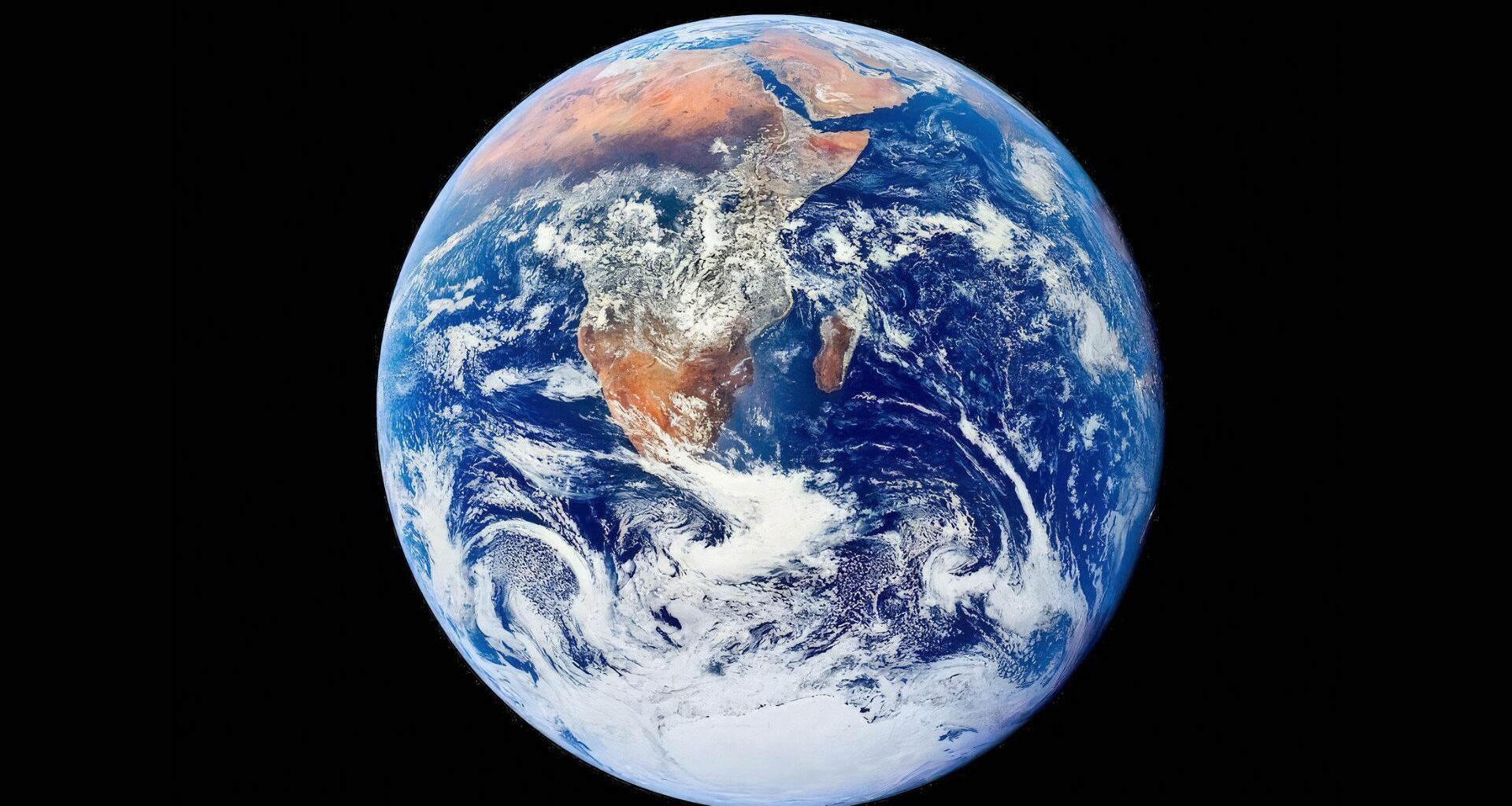 A blue and white sphere with brown continents on it is seen in the darkness of space.