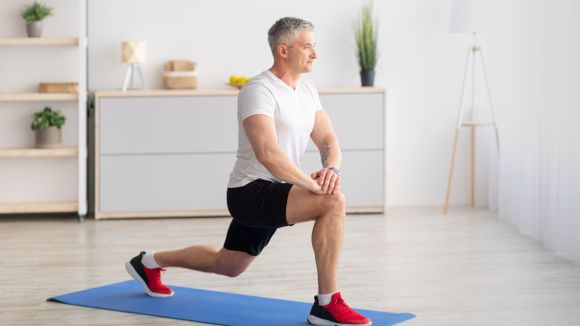 Older man at home lunging on a yoga mat