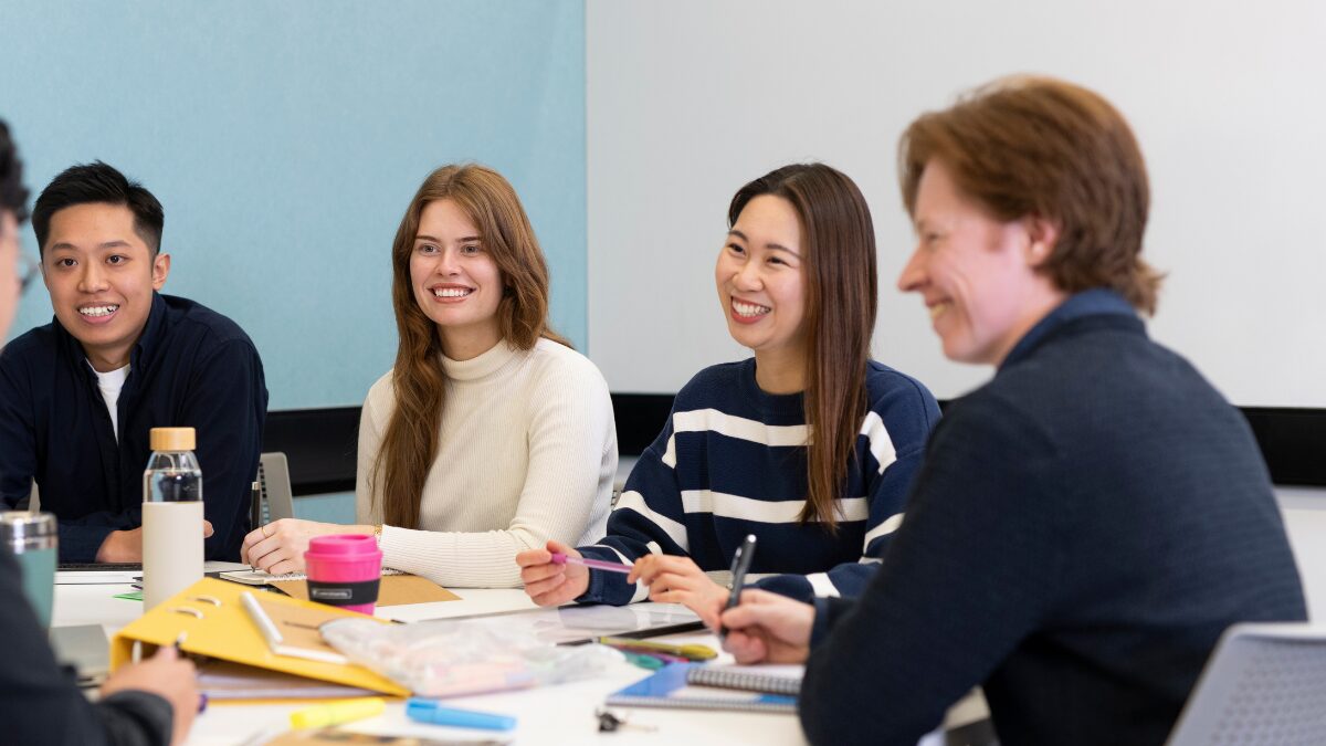 Group of university students sitting around a table, smiling and talking during a collaborative class activity.