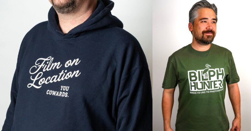 Two men stand side by side. One wears a navy hoodie with “Film on Location You Cowards.” The other wears a green T-shirt reading “BIRD HUNTER Birds I’d Like to Photograph” with a bird graphic above the text.