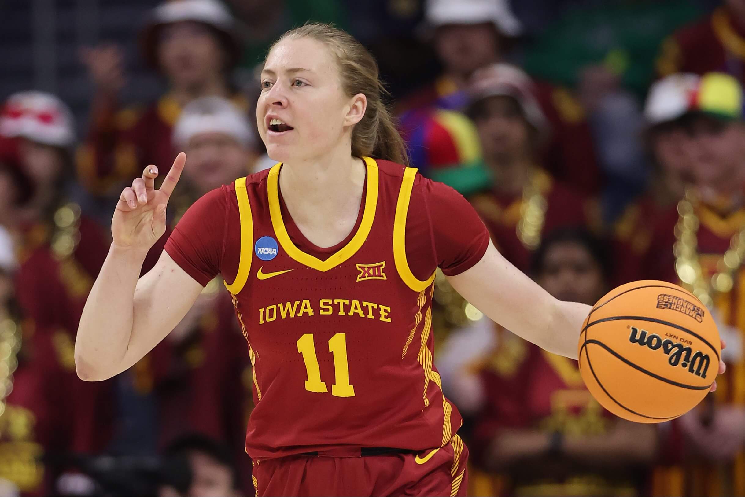 An image of former Iowa State women's basketball player Emily Ryan dribbling the ball with her left hand and signaling a play with her right hand during an NCAA basketball game.