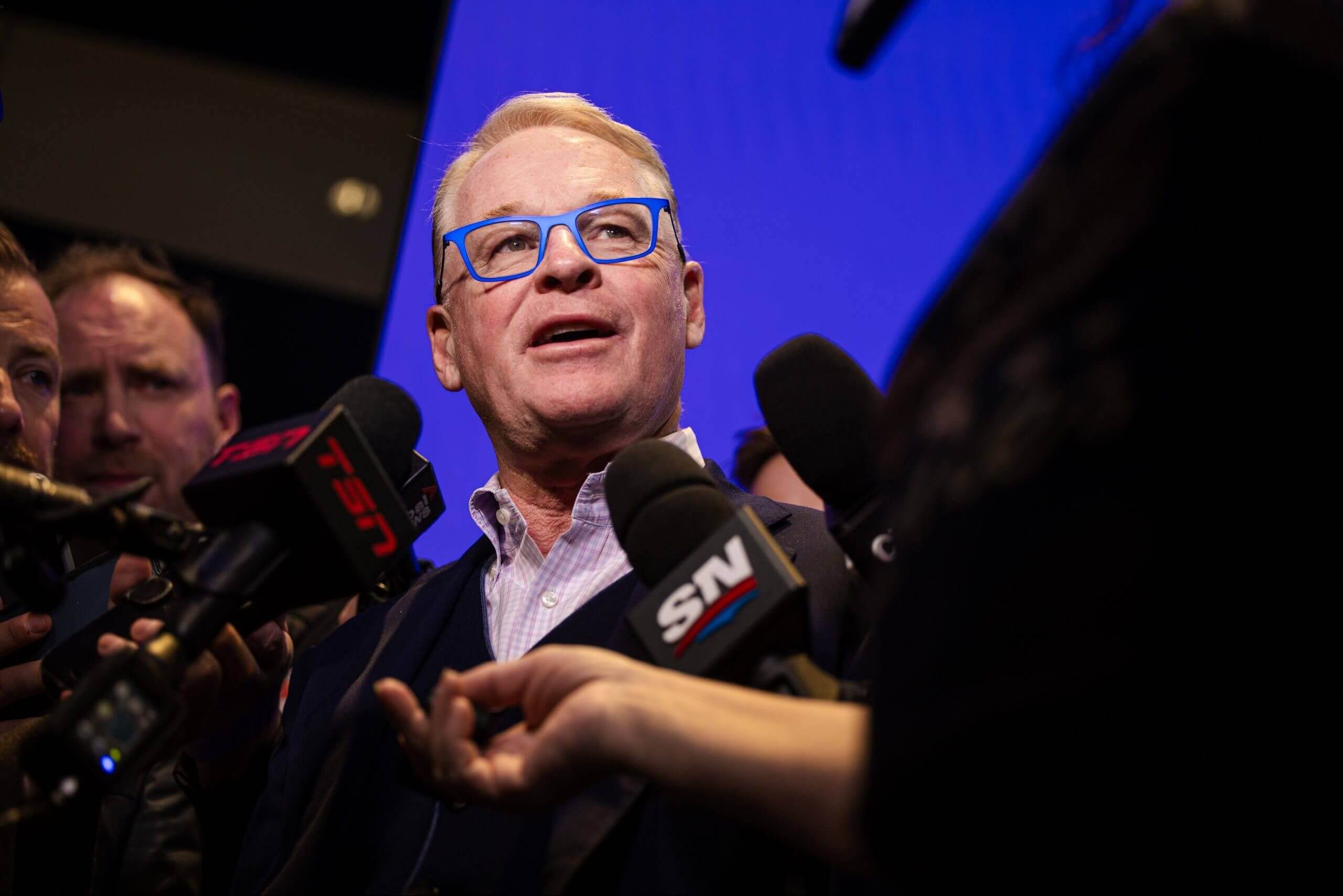 Keith Pelley answers questions with several microphones being held in front of him by reporters.