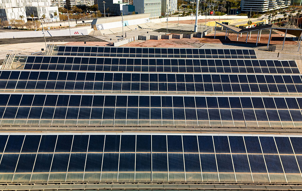 Rows of large solar panels sit on the ground in an industrial area.