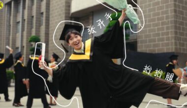 A person holds a smartphone showing an augmented reality outline of a graduate in cap and gown. In the background, people in graduation attire stand outside a building.